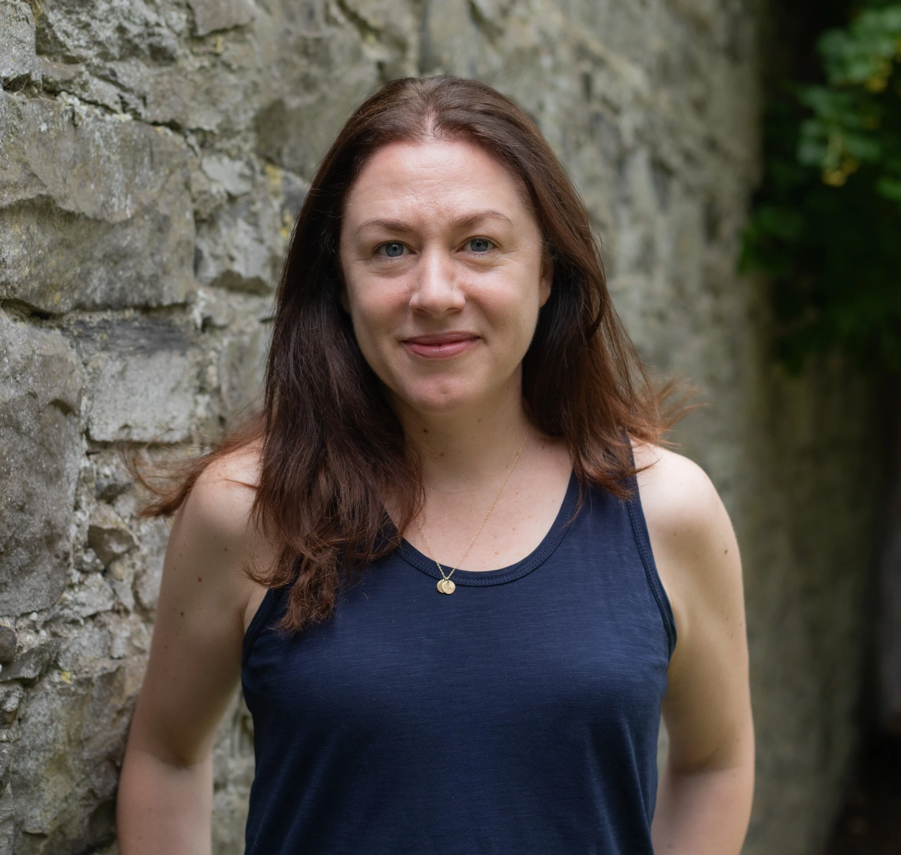 Portrait of Caitríona Lally beside a stone wall